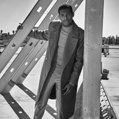Shane is posing wearing a trench coat in this monochrome picture. 